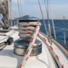 Braided white and red polyester rope (ROPIRA PES Sail) wrapped around a stainless steel winch on a sailboat deck, with the ocean and mast lines in the background.
